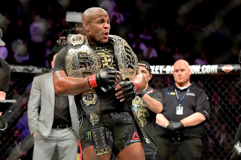 Daniel Cormier holding two championship belts inside the octagon