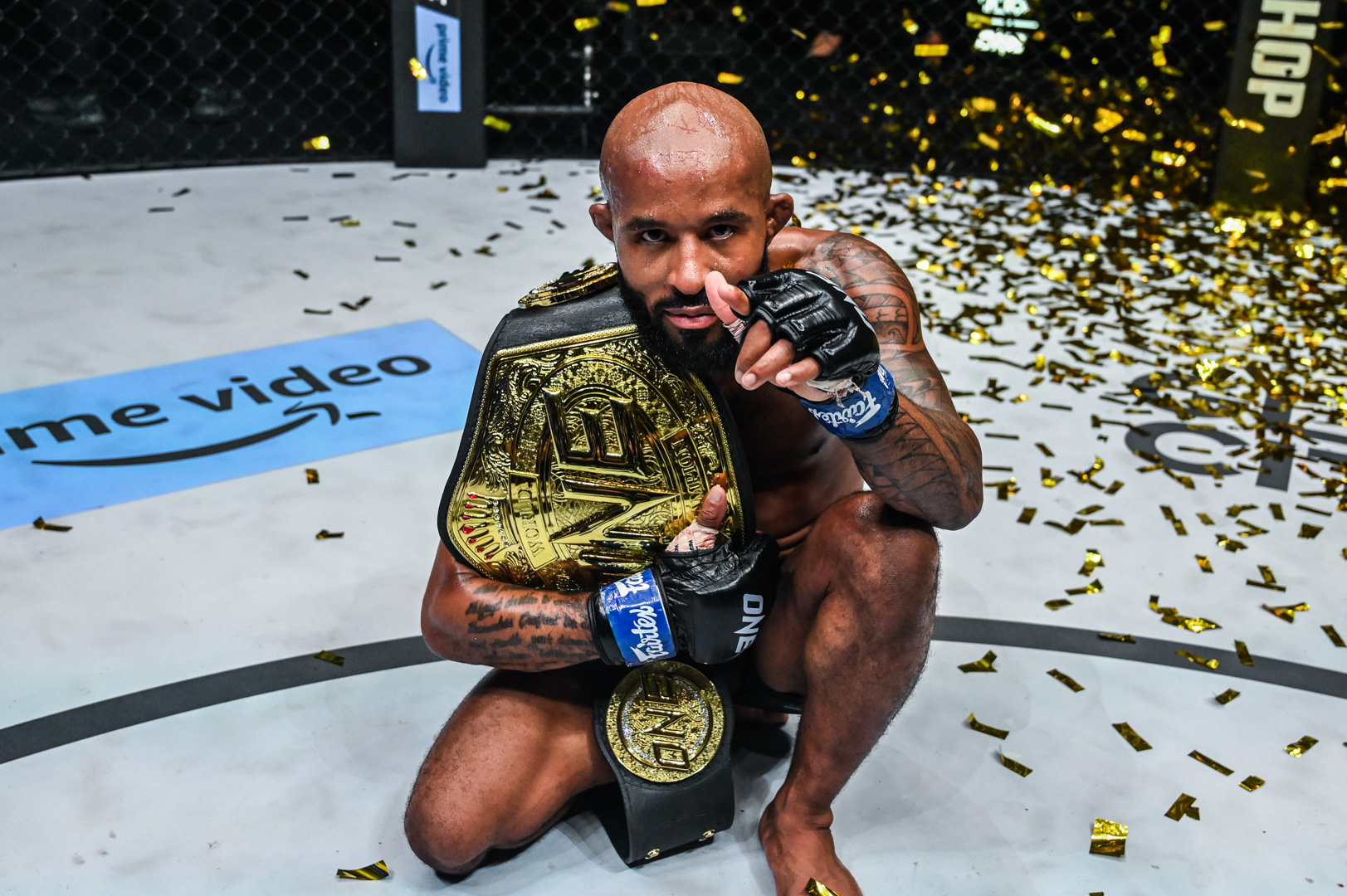 Demetrious Johnson kneeling with a championship belt amid gold confetti
